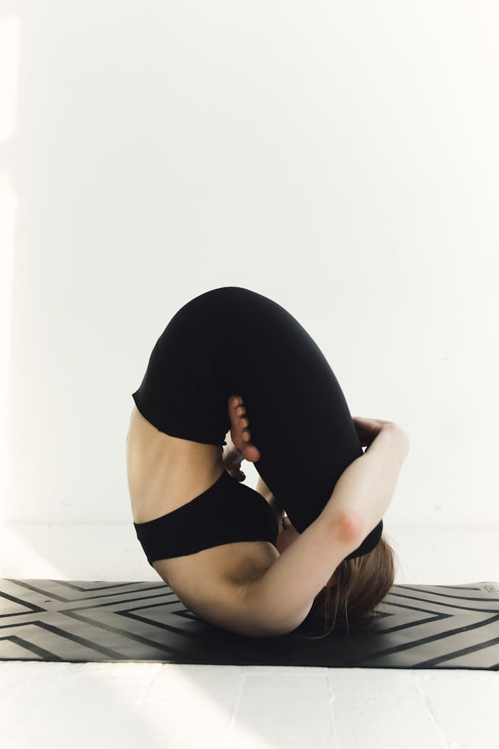 A woman in activewear performs a challenging yoga pose on a mat indoors, showcasing flexibility and mindfulness.