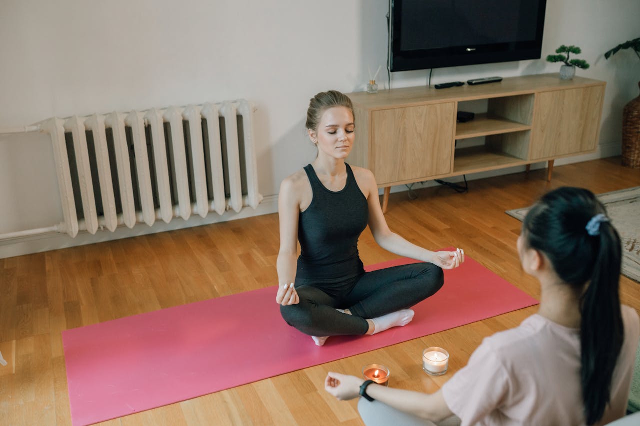 Two women meditating on a yoga mat indoors, practicing mindfulness and relaxation.